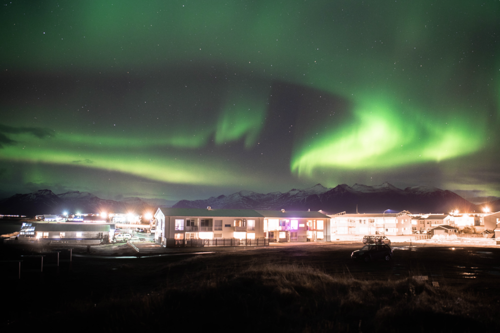 Swirly, Green Northern Lights over a mountain and some buildings