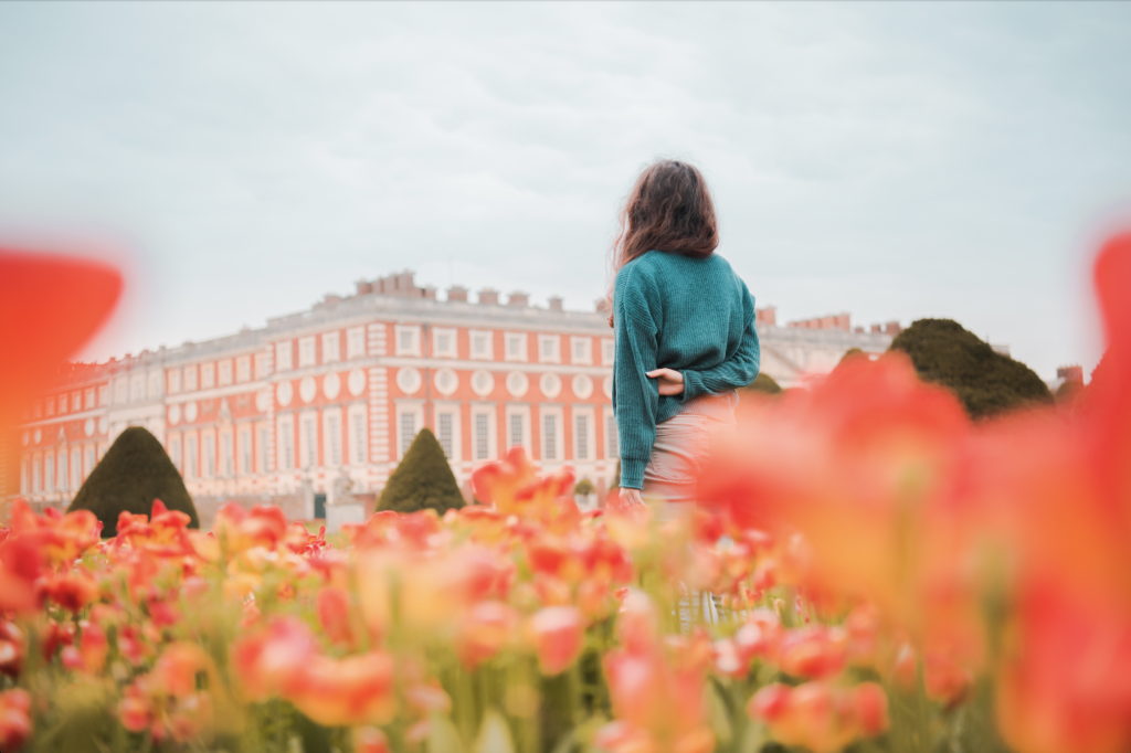 A girl in turquoise sweater standing in red tulips outside of Hampton Court Palace